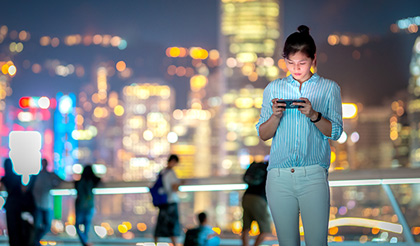 Asian woman looking at her phone with a city skyline in the background
