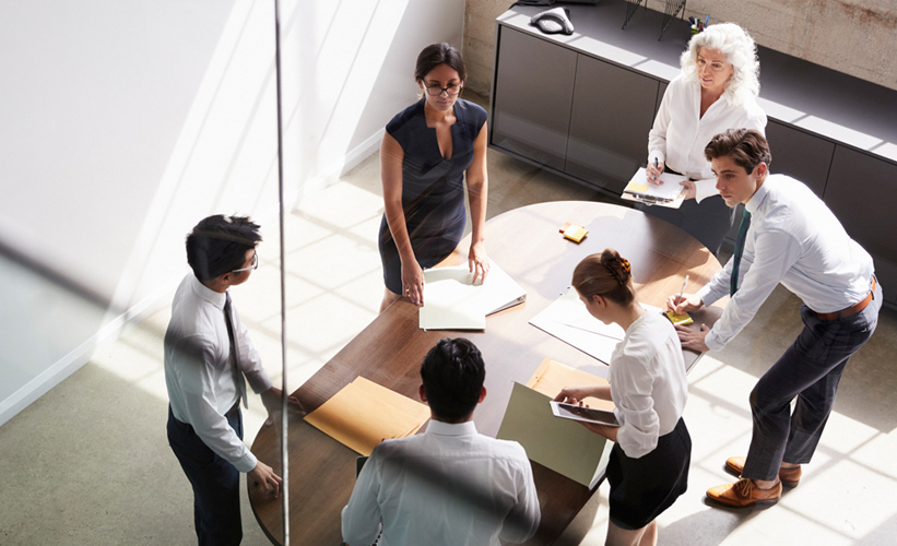 A group of people standing around a desk in the office 