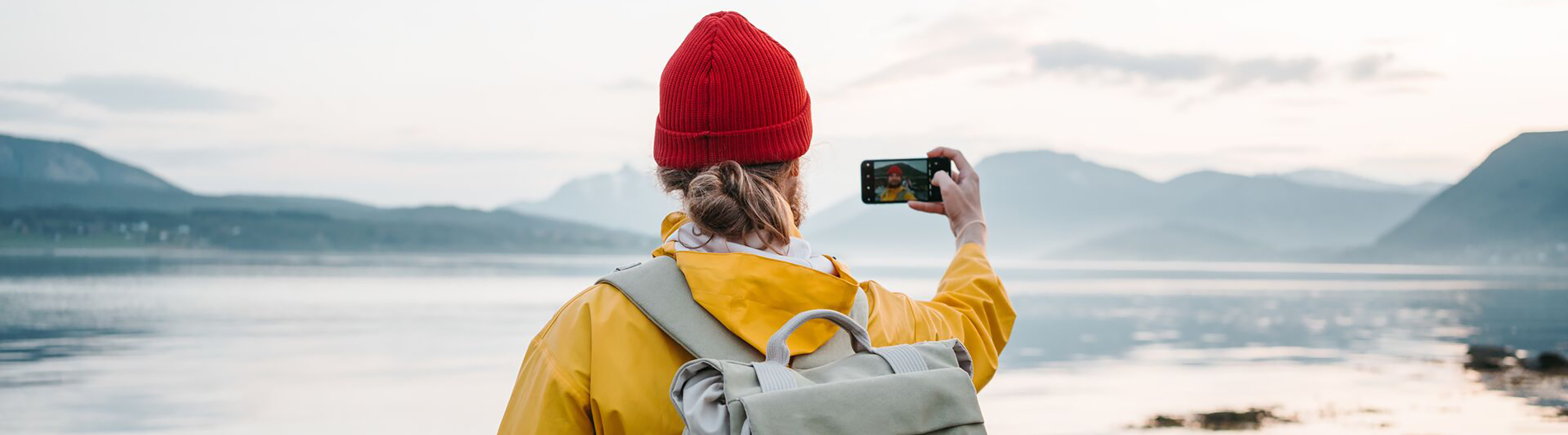 Man taking a selfie in front of a lake surrounded by mountains