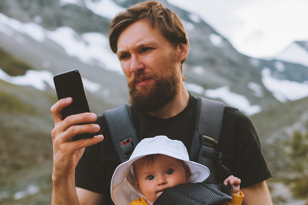 Man with a baby in the mountains browsing on his phone