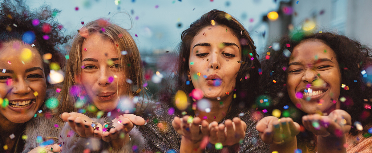 Four women smiling and blowing colorful confetti