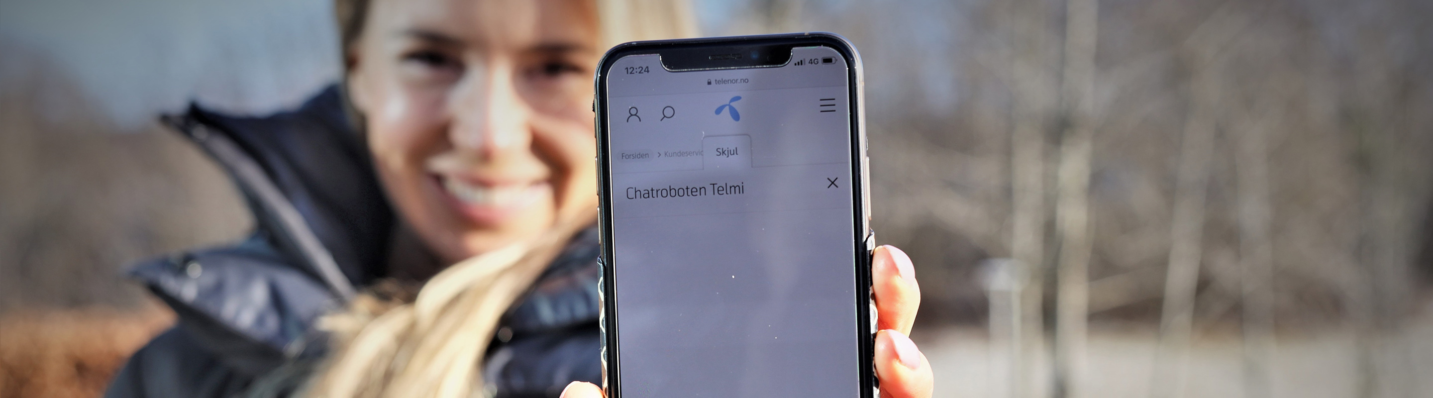 Woman holding a phone displaying the Telmi chatbot from Telenor Norway