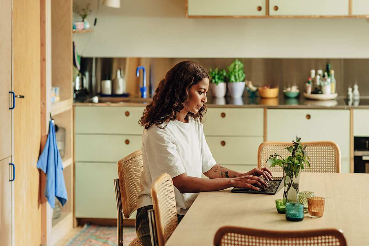 Person skriver på en bærbar PC i et lyst kjøkkenmiljø