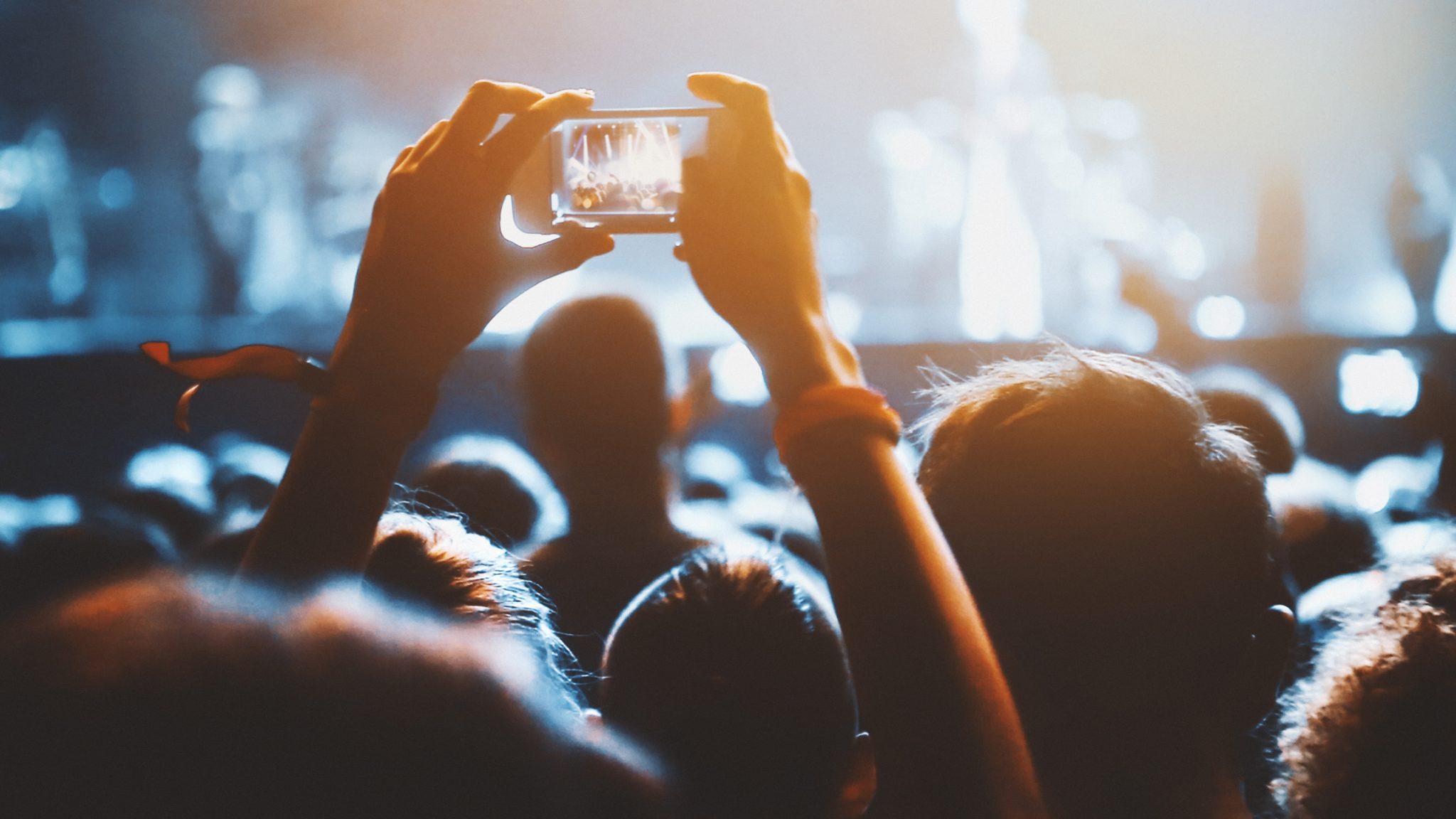 Person taking a picture with a phone at a concert surrounded by people