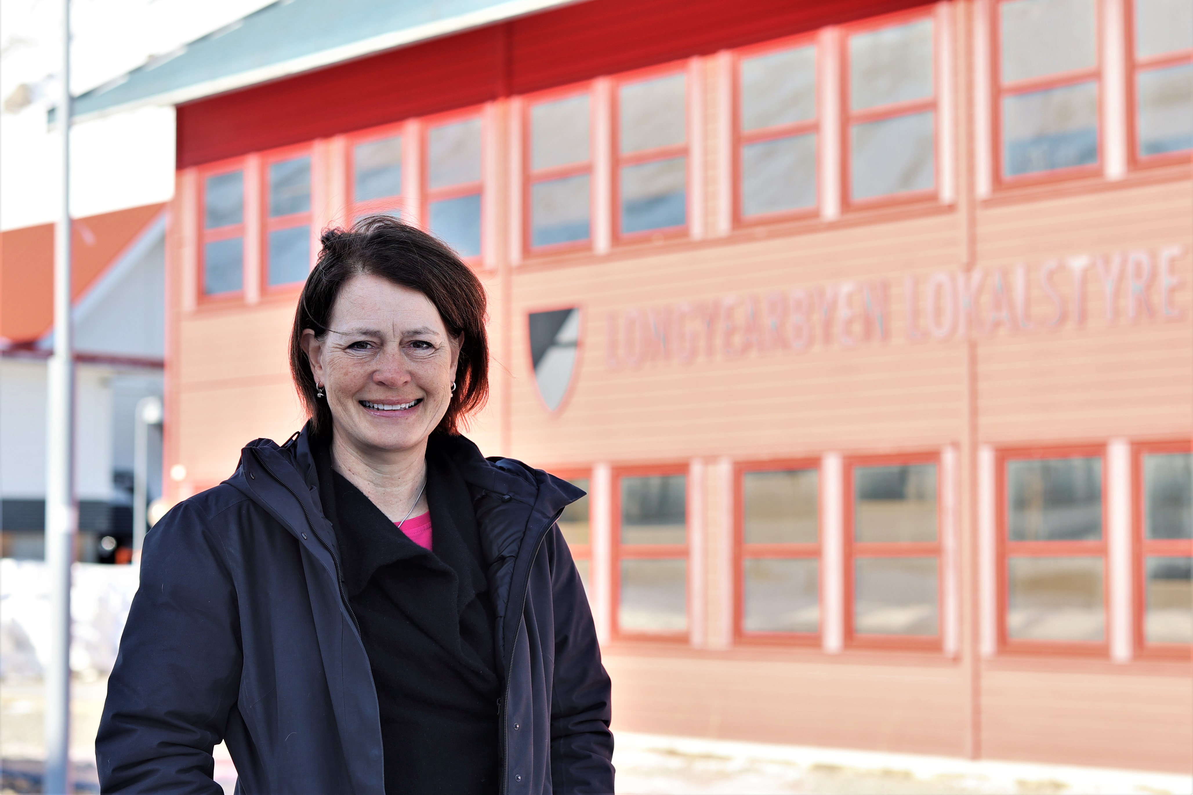 Woman standing outside a red building looking towards the camera.