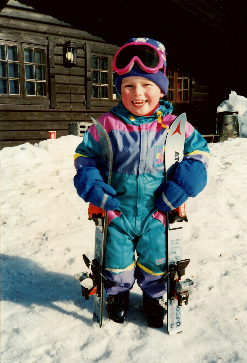 Barn i fargerik skidress foran snødekt trehytte